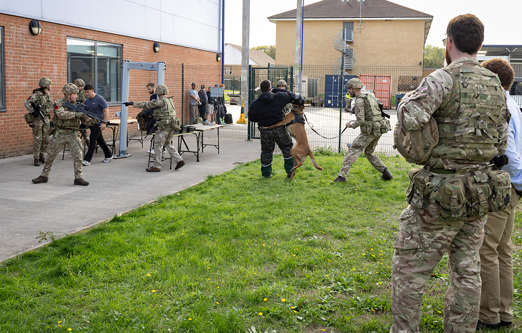 MinVP observes passenger processing during an operational training scenario. An explosives and arms detection dog detected a passenger smuggling weapons. As RAF Police personnel move to investigate, the passenger attempts to flee the scene but is swiftly detained by an RAF Police Military Working Dog (MWD) team. The individual is subsequently arrested while MinVP watches the exercise demonstrating RAF Police operational capabilities.
